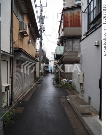 縱橫交錯的昏暗狹窄的小巷,蜿蜒於城市建築和鏽跡斑斑的波紋鐵皮牆之間。 縱橫交錯的昏暗狹窄的小巷,蜿蜒於城市建築和鏽跡斑斑的波紋鐵皮牆之間。 132655816