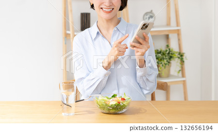 A woman eating while watching a smartphone A woman eating while watching a smartphone 132656194