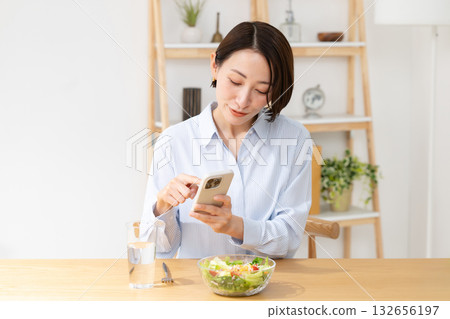 A woman eating while watching a smartphone A woman eating while watching a smartphone 132656197