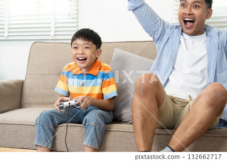 Joyful Family Moments and Gaming. A father and son share laughter during a gaming session in their cozy living room. 132662717