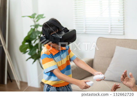 Family Fun and Virtual Reality. A child engaging in virtual reality gaming with excitement in a cozy living room. 132662720