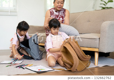 Back to School Excitement. Two girls sorting their school supplies and packing their backpacks with their grandmother's help. Back to School Excitement. Two girls sorting their school supplies and packing their backpacks with their grandmother's help. 132662762