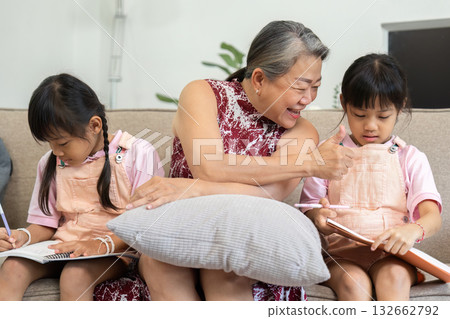 Learning and Bonding. A grandmother engages with her granddaughters as they work on their school activities. 132662792