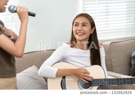 Musical Moments and Family Fun. A mother playing guitar while her daughter sings, creating a joyful atmosphere. Musical Moments and Family Fun. A mother playing guitar while her daughter sings, creating a joyful atmosphere. 132662926