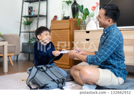 Father and son sharing a joyful moment while packing school supplies 132662932