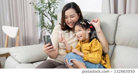 Family Joy and Screen Time. A mother and daughter share a lighthearted moment while looking at a smartphone. 132663050