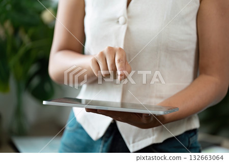 Touchscreen Technology and User Engagement. A woman interacting with a tablet, demonstrating modern digital skills in a casual setting. Touchscreen Technology and User Engagement. A woman interacting with a tablet, demonstrating modern digital skills in a casual setting. 132663064