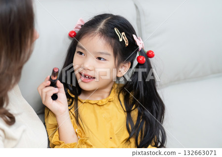 Family Moments and Playful Imagination. A daughter shares her excitement as she plays with makeup alongside her mother. Family Moments and Playful Imagination. A daughter shares her excitement as she plays with makeup alongside her mother. 132663071