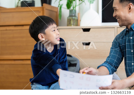 Back to School and Engaging Learning. A father and son share smiles while reviewing school materials at home. Back to School and Engaging Learning. A father and son share smiles while reviewing school materials at home. 132663139