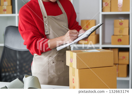 Entrepreneurship and E-commerce. An entrepreneur meticulously taking notes while managing online sales shipments. 132663174