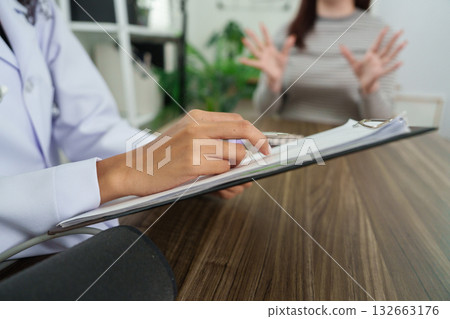 Consultation and Patient Engagement. A doctor attentively takes notes during a patient's consultation, ensuring a thorough examination of health concerns. 132663176
