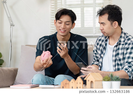 Loving LGBTQ couple discussing savings strategies while sitting on a couch at home. Financial planning and budgeting for a secure future in a cozy living space. Loving LGBTQ couple discussing savings strategies while sitting on a couch at home. Financial planning and budgeting for a secure future in a cozy living space. 132663186