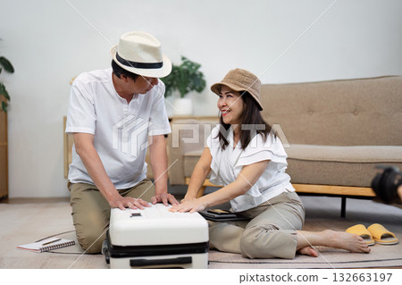 Elderly Asian couple smiling while packing a suitcase together, wearing hats and enjoying the travel preparation experience. Elderly Asian couple smiling while packing a suitcase together, wearing hats and enjoying the travel preparation experience. 132663197