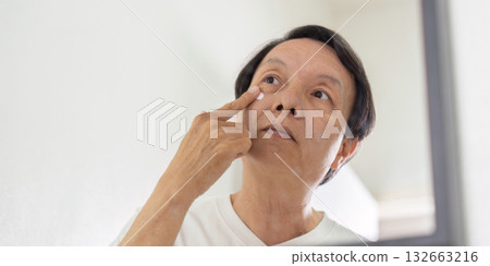Elderly Skincare Routine. An older man applying cream to his face in front of a mirror. 132663216