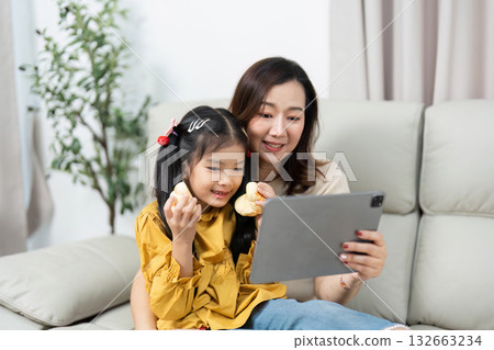 Family Connection and Digital Interaction. A mother and daughter enjoy watching something together on a tablet. Family Connection and Digital Interaction. A mother and daughter enjoy watching something together on a tablet. 132663234