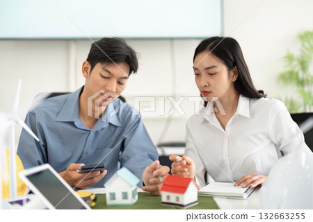 Sustainability and Engineering. Two engineers discussing sustainable building designs using miniature models in a modern office setting. Sustainability and Engineering. Two engineers discussing sustainable building designs using miniature models in a modern office setting. 132663255