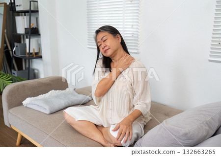 Health and Comfort. An elderly woman sitting on a couch, gently holding her shoulder while sitting comfortably. Health and Comfort. An elderly woman sitting on a couch, gently holding her shoulder while sitting comfortably. 132663265