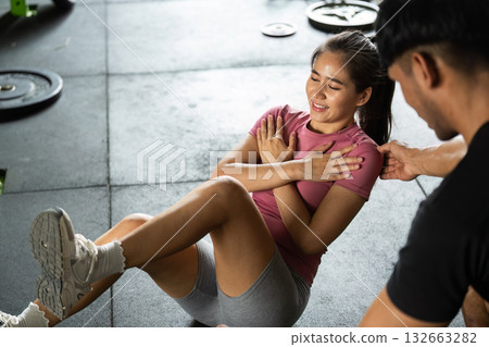 Workout session with personal trainer assisting female client in gym Workout session with personal trainer assisting female client in gym 132663282