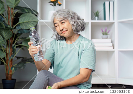 Thoughtful senior woman examining a water bottle, reflecting on hydration and wellness. Thoughtful senior woman examining a water bottle, reflecting on hydration and wellness. 132663368