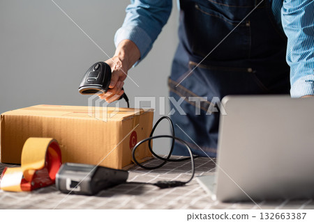 E-commerce entrepreneur scanning a package with a barcode scanner at a workspace, preparing for online selling and shipping. 132663387