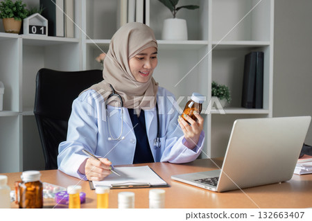 Engaged Muslim female doctor reviewing medication and taking notes in her modern office, emphasizing healthcare and patient education. Engaged Muslim female doctor reviewing medication and taking notes in her modern office, emphasizing healthcare and patient education. 132663407