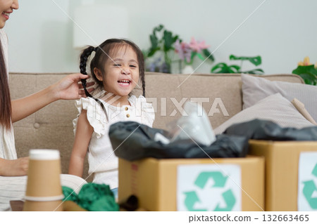 Recycling and Childhood Joy. A little girl smiles as she engages in a recycling project with family. 132663465