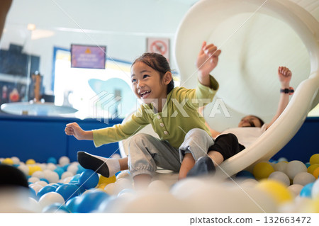 Exciting Slide Adventure. Happy girl sliding down into colorful ball pit, expressing joy and excitement. Exciting Slide Adventure. Happy girl sliding down into colorful ball pit, expressing joy and excitement. 132663472