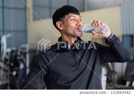 Hydration and Fitness. Man drinking water after exercise in a gym environment. Hydration and Fitness. Man drinking water after exercise in a gym environment. 132663482