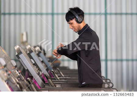 Workout and Fitness. Smiling man checking smartwatch while using treadmill in a gym. Workout and Fitness. Smiling man checking smartwatch while using treadmill in a gym. 132663483