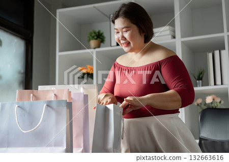 Happy woman unpacking shopping bags at home after a successful shopping trip. 132663616