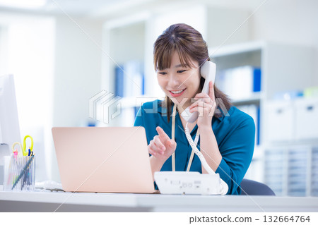Business woman talking on the phone while looking at a computer Business woman talking on the phone while looking at a computer 132664764