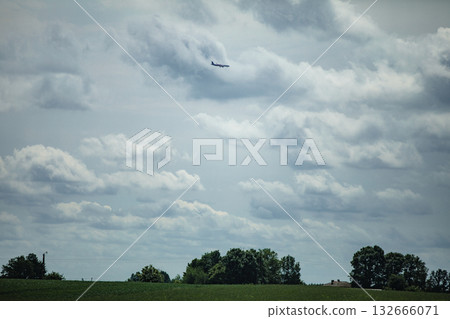 A majestic plane gracefully gliding through the scenic green fields beneath dramatic skies 132666071