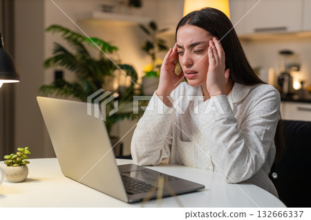 Young woman rubs temples eye strain from laptop screen takes break then resumes work tired evening 132666337