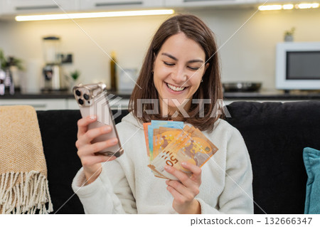 Woman counts euro money cash checks rate on smartphone smiles plans dream buy salary savings bonus 132666347