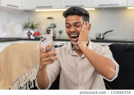 Indian man reads message on smartphone smiles makes victory gesture big thumbs up celebrates triumph Indian man reads message on smartphone smiles makes victory gesture big thumbs up celebrates triumph 132666356
