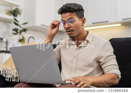 Indian man puts on glasses for clear reading of small notebook text vision focus resumes daily work 132666368