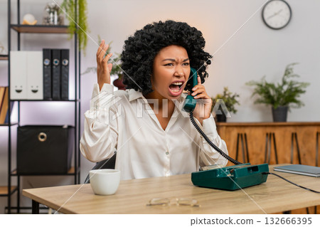 African American businesswoman yells on retro phone waving hand frustrated during angry dispute call African American businesswoman yells on retro phone waving hand frustrated during angry dispute call 132666395