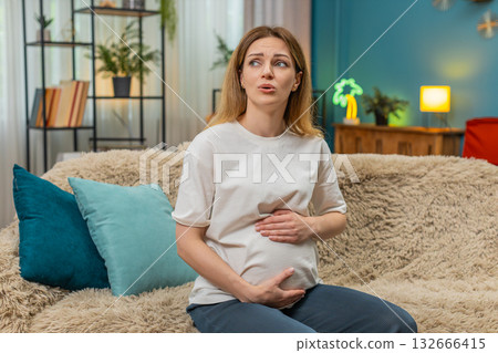 Pregnant woman holds belly breathes during mild contractions smiles listens to baby movement on sofa 132666415