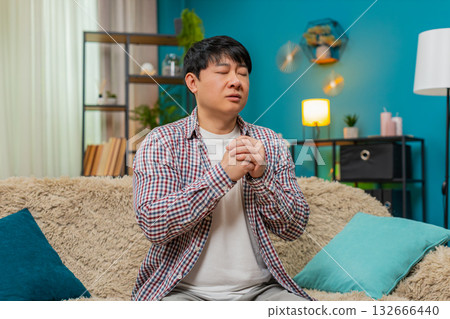 Asian man with eyes closed repeating mantra, calm meditative prayer, hopeful quiet spiritual moment 132666440