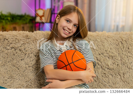 Child girl kid playing alone on sofa at home tossing basketball ball in air enjoying solo indoor fun 132666484