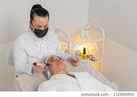 Cosmetologist doing peeling procedure, woman skin regeneration, dermapen microneedling, dermastamp Cosmetologist doing peeling procedure, woman skin regeneration, dermapen microneedling, dermastamp 132666950