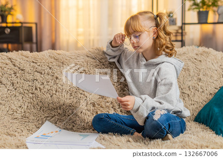 Young teenager girl wearing glasses at home sofa studying documents and receipts serious expression Young teenager girl wearing glasses at home sofa studying documents and receipts serious expression 132667006