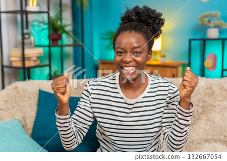 African American woman celebrating victory sofa jumping hands raised joyful energy success indoors 132667054