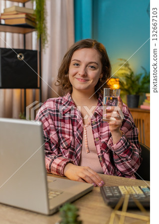 Businesswoman girl sitting at workplace desk drinking water while working with laptop in home office 132667103