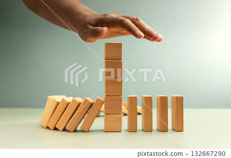 Hand stopping falling dominoes, Economic crisis prevention 132667290