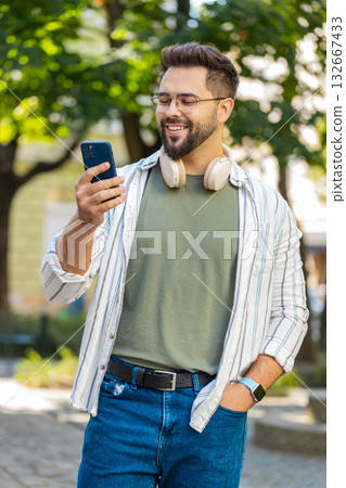 Smiling young man using smartphone typing texting scrolling social media app on city town street 132667433