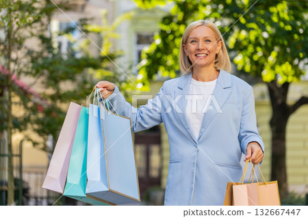 Mature businesswoman in suit carrying shopping bags while walking on city street after purchases 132667447