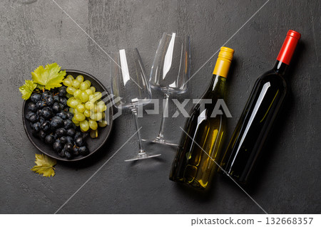 Red and white wine bottles with a glass and bowl of fresh grapes 132668357
