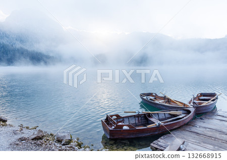 Wooden boats by the pier on a lake at sunset with mist rising over the water 132668915