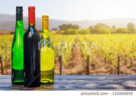 Wine bottles with grapes on a wooden table, glowing with sunny vineyard bokeh in the background Wine bottles with grapes on a wooden table, glowing with sunny vineyard bokeh in the background 132668956